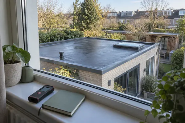 Een rechthoekig uitbouwdak vanuit een veilig raam, met meetgereedschap op de vensterbank.